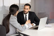 © fizkes - Team members working on business task during teamwork in office boardroom, share ideas, planning strategic decision, discussing report result, explain solution, speaking, sitting at table with laptop