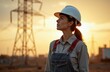 © Pete - Woman worker with hard hat looks up at sunset near power lines. She wears denim overalls, stands in industrial area, ready for her next job assignment.