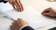 © KHIAR.PROJECTS - Two individuals engage in a professional exchange, with one person handing a blank document to another across a clean, bright desk surface, symbolizing agreement or transfer.