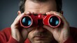 © DSimage - Close up portrait of man looking through red binoculars, concept of vision, search, focus and future planning on dark background.