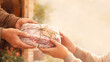 © M - Hands exchanging a beautifully wrapped package of raw meat with a 'From our family to yours' tag, bathed in warm golden light.