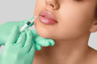 © Pixel-Shot - Young woman receiving lip injection on grey background, closeup