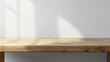 © letter - Minimal wooden tabletop against a white textured wall bathed in soft sunlight with gentle window shadows, creating a calm and serene empty interior scene