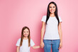 © deagreez - Mother and daughter holding hands and smiling together in casual white t-shirts against a pink background family portrait of parent and child connection