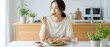 © SIMANG - Young woman eating fresh salad at kitchen table in a bright and healthy home setting