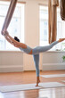 © golubovy - Flexibility training. Body balance. Woman in sportswear doing aerial yoga exercise standing on tiptoe leaning forward holding hammock in studio.