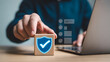 © Shawon003 - Hand placing wooden block with checkmark and shield icon on laptop.