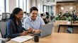 © Eve - Happy diverse business team laughing while working on laptop in office. African American woman and Hispanic man collaborating, positive work environment, creative agency and teamwork.