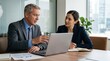 © Eve - Senior businessman mentoring young female colleague during laptop meeting. Professional male manager explaining data and strategy to woman in corporate boardroom office.