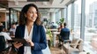 © Eve - Portrait of happy curly hair businesswoman holding tablet in busy open plan office. Modern female executive, diverse leadership and successful management in tech company.