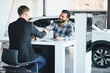 © Serhii - Client and salesman shaking hands sealing car deal at dealership