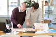 © JackF - Young and elderly men at table in office discussing and drawing building construction plan on large sheet of paper