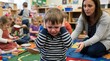 © David - Upset little boy covering his ears and crying in a colorful preschool classroom while a caring teacher tries to comfort him