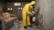 © David - Professional in yellow hazmat suit spraying mold on a concrete basement wall during a hazardous remediation and cleaning process.