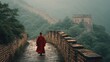 © Envision - Rear view of a solitary person in a red cloak walking on the ancient Great Wall of China, surrounded by green mountains and foggy atmosphere at dawn