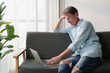 © Tj - Mature man dealing with work challenges and stress while telecommuting from home, using a laptop, showing dedication and focus in a casual setting