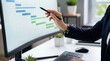 © remake - Business professional pointing at gantt chart project schedule with pen stylus on curved monitor at office desk. Management timeline task planning and workflow tracking software for strategy