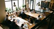© ELENA - Overhead view of creative professionals working on laptops at communal wooden tables in a bright cafe with industrial pendant lights, potted plants, and menu board.