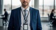 © Tatiana - Businessman in suit wearing lanyard with ID badge in modern office. Professional male employee standing in corporate workplace. Formal attire and corporate identity for business meeting.