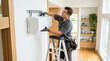 © akridiy - HVAC installer man mounting mini-split air conditioning unit on residential wall