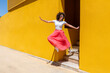 © VISTA by Westend61 - Happy woman with arms outstretched jumping from steps near yellow wall