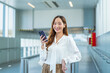 © StockPhotoRepublic - Asian Businesswoman holding smartphone and smiling at camera in airport walkway