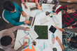 © deagreez - Young professionals collaborating in a creative business meeting around a table with laptops, charts, coffee and a living moss centerpiece