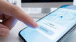 © Bagas - Close-up of a Finger Pressing Track Delivery Button on Smartphone App Interface with Real-Time Map and Package Shipping Status in Office