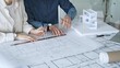 © volha_r - Architects working together, developing a building design by assembling a scale model and reviewing detailed blueprints, symbolizing teamwork, planning, and architectural creation