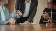 © Phushutter - Business meeting with lawyer and clients at wooden table, discussing documents with judge gavel and scales in foreground, concept of legal consultation and negotiation.