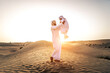 © oneinchpunch - Arabian man and son playing in the desert at sunset - Middle-eastern father and his kid wearing traditional emirati kandura spending time together in Dubai desert