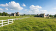© vefimov - A serene view of a stone castle nestled among verdant fields under a bright sky. The castle's rustic charm is complemented by a white wooden fence.