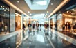 © Sg - A blurred, expansive view of a modern shopping mall interior showcases a bustling atmosphere with numerous stores and shoppers.