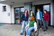 © Halfpoint - Group of teenage students supporting friend in wheelchair in front of school building.