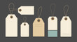 © Fahima - Variety of blank paper gift tags and price labels in different shapes and sizes hanging from strings on a dark gray background.