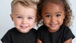 © Nick Freund - Zwei lächelnde Kleinkinder – ein helles und ein dunkelhäutiges – in schwarzen T-Shirts vor weißem Hintergrund