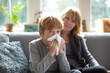 © AI_images - Boy holding tissue and sitting beside mother on sofa, caring parenting moment during mild illness, bright cozy home interior, natural window light