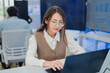 © whyframeshot - professional female software developer with glasses sitting at her desk, holding a coffee cup while intently working on her laptop. The scene captures a modern business environment