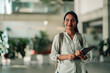 © Zamrznuti tonovi - Young indian student smiling and carrying backpack and digital tablet in a modern university campus building