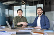 © Liubomir - Two smiling multi-ethnic businessmen are shaking hands across a conference table in a modern office, signifying a successful partnership and agreement during a business meeting