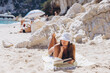 © anatoliycherkas - Woman relaxing at Cala Luna beach in Sardinia, reading a book enjoying a summer beach vacation in Italy