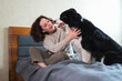 © Юлия Завалишина - Smiling woman playing with cute puppy dog border collie on bed at home indoor. Owner girl stroking holding dog friend sitting on sofa in living room. Love for pets friendship support team concept