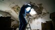 © Creatify_Tech - Construction worker repairing leaking ceiling inside dark attic space with wooden roof support beam.