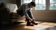 © BUDI - A man sits on a couch tying his shoes.  Sunlight streams through a window