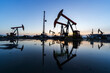 © zhengzaishanchu - in the evening, oil pumps are running, The oil pump and the beautiful sunset reflected in the water, the silhouette of the beam pumping unit in the evening.