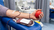 © Mary - Close-up of a male donor's arm as he donates blood in a hospital, holding a red stress ball during the process.