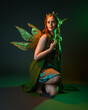 © faestock - portrait of female model wearing fantasy fairy costume, green dress, cloak, butterfly wings and crown. full length sitting pose, kneeling on floor, dark studio background.