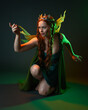 © faestock - portrait of female model wearing fantasy fairy costume, green dress, cloak, butterfly wings and crown. full length sitting pose, kneeling on floor, dark studio background.