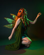 © faestock - portrait of female model wearing fantasy fairy costume, green dress, cloak, butterfly wings and crown. full length sitting pose, kneeling on floor, dark studio background.