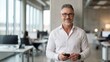 © nyul - Confident, successful middle aged businessman in office. Portrait of happy mid adult man smiling. Mature entrepreneur standing in corporate workspace. Senior male in white business shirt.